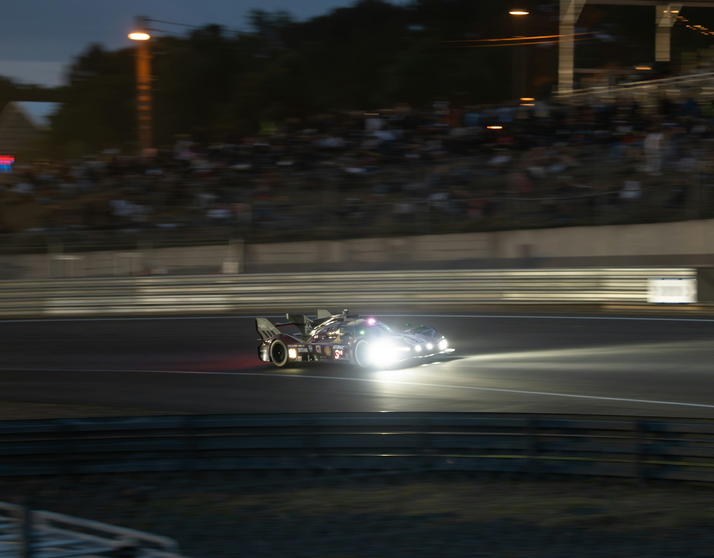 A prototype race car at night, headlights on, rounding a dark corner under track lights